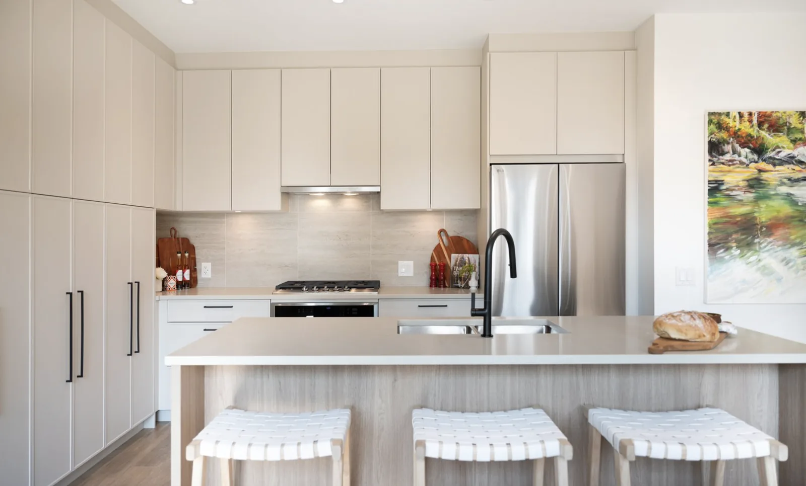 Kitchen in a Beaumont display home — two-toned cabinetry with matte-black pulls, engineered stone island, five-burner gas cooktop and stainless steel appliances