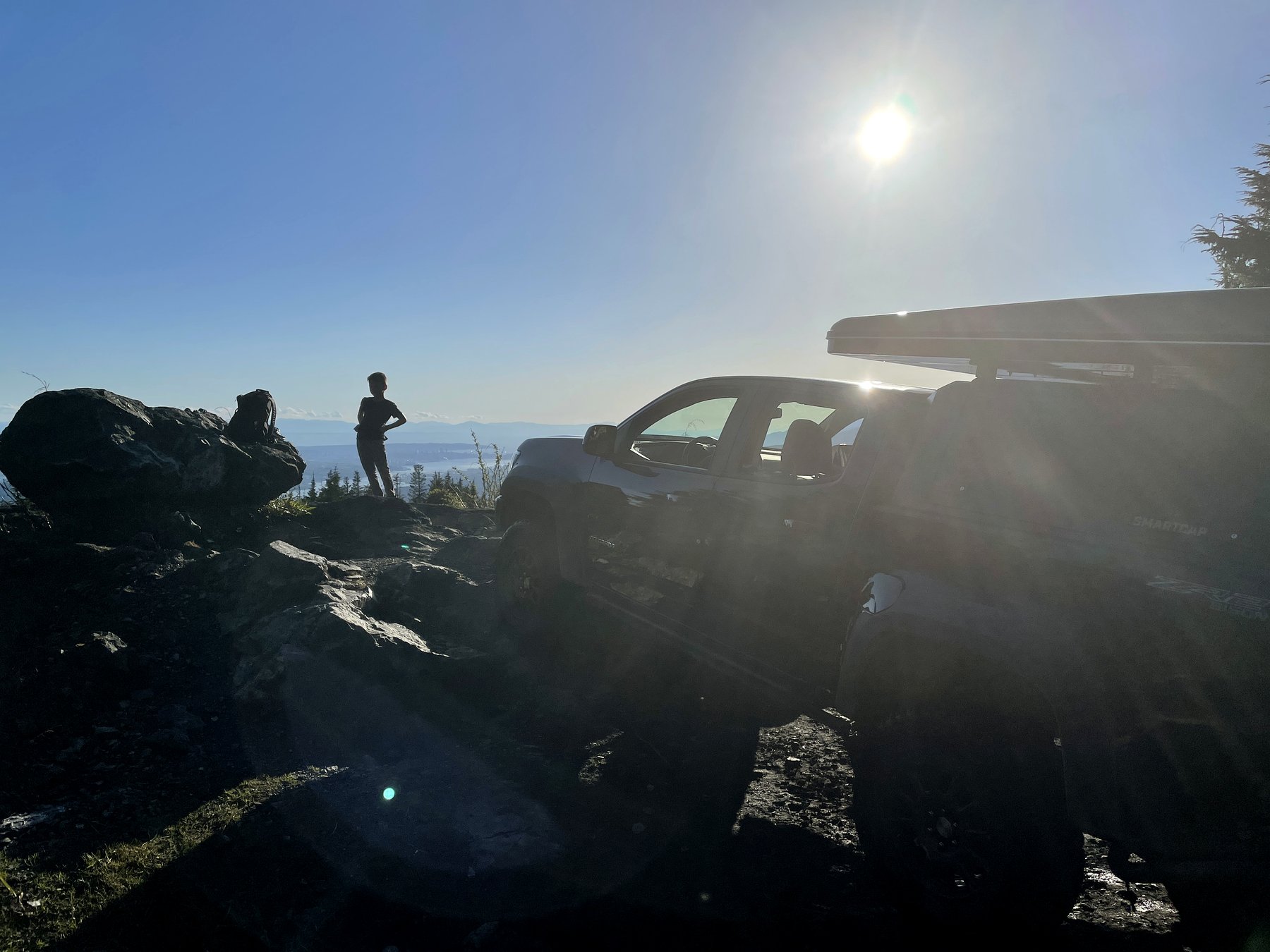 A 4x4 vehicle on the Eagle Mountain access road in Coquitlam, BC, with sun flare and forest visible — the kind of vehicle that residents use to access the upper mountain after receiving City of Coquitlam approval.