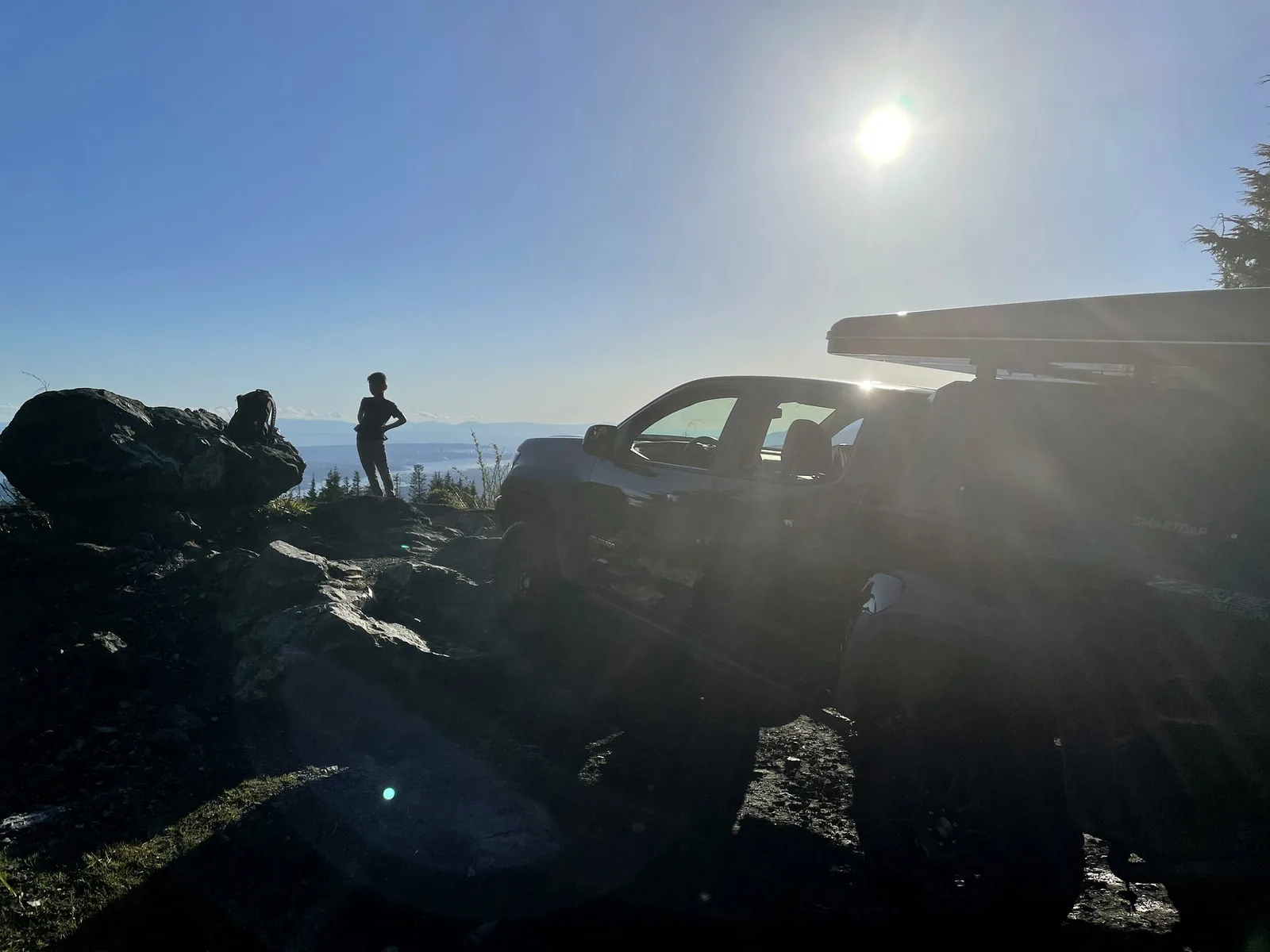 A 4x4 vehicle on the Eagle Mountain access road in Coquitlam, BC, with sun flare and forest visible — the kind of vehicle that residents use to access the upper mountain after receiving City of Coquitlam approval.