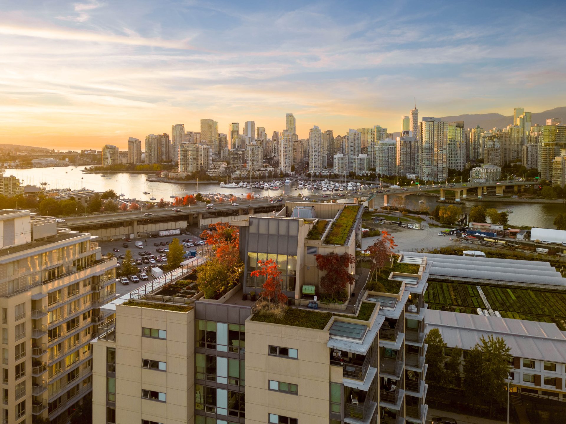Aerial view of JAMES at sunset showing its green rooftop terraces, False Creek, and the full downtown Vancouver skyline