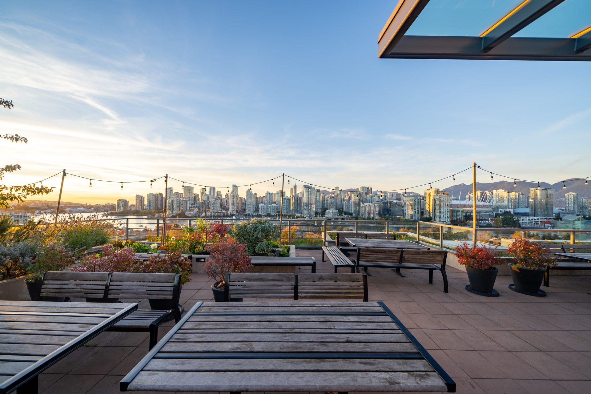 Rooftop terrace at JAMES at sunset with lounge seating, string lights, planters, and the downtown Vancouver skyline in the distance