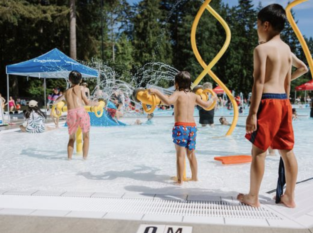 Mundy Park Pool exterior with the renewed deck, sunbathing lawn, and forest backdrop in Coquitlam.