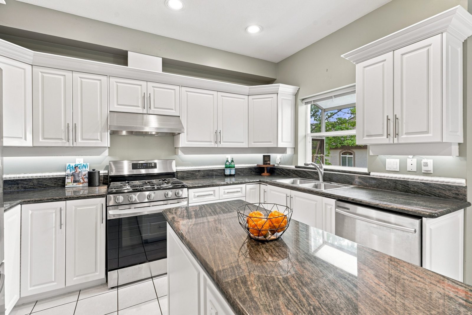 Kitchen with white cabinetry, dark granite counters, island and gas range at #11 915 Fort Fraser Rise