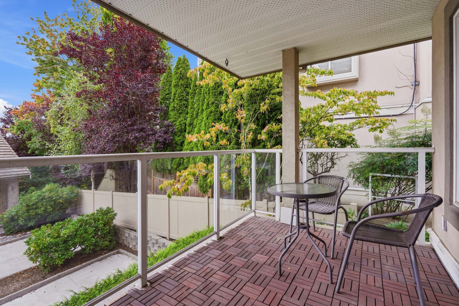 Covered balcony with glass railing overlooking trees and hedges at #11 915 Fort Fraser Rise